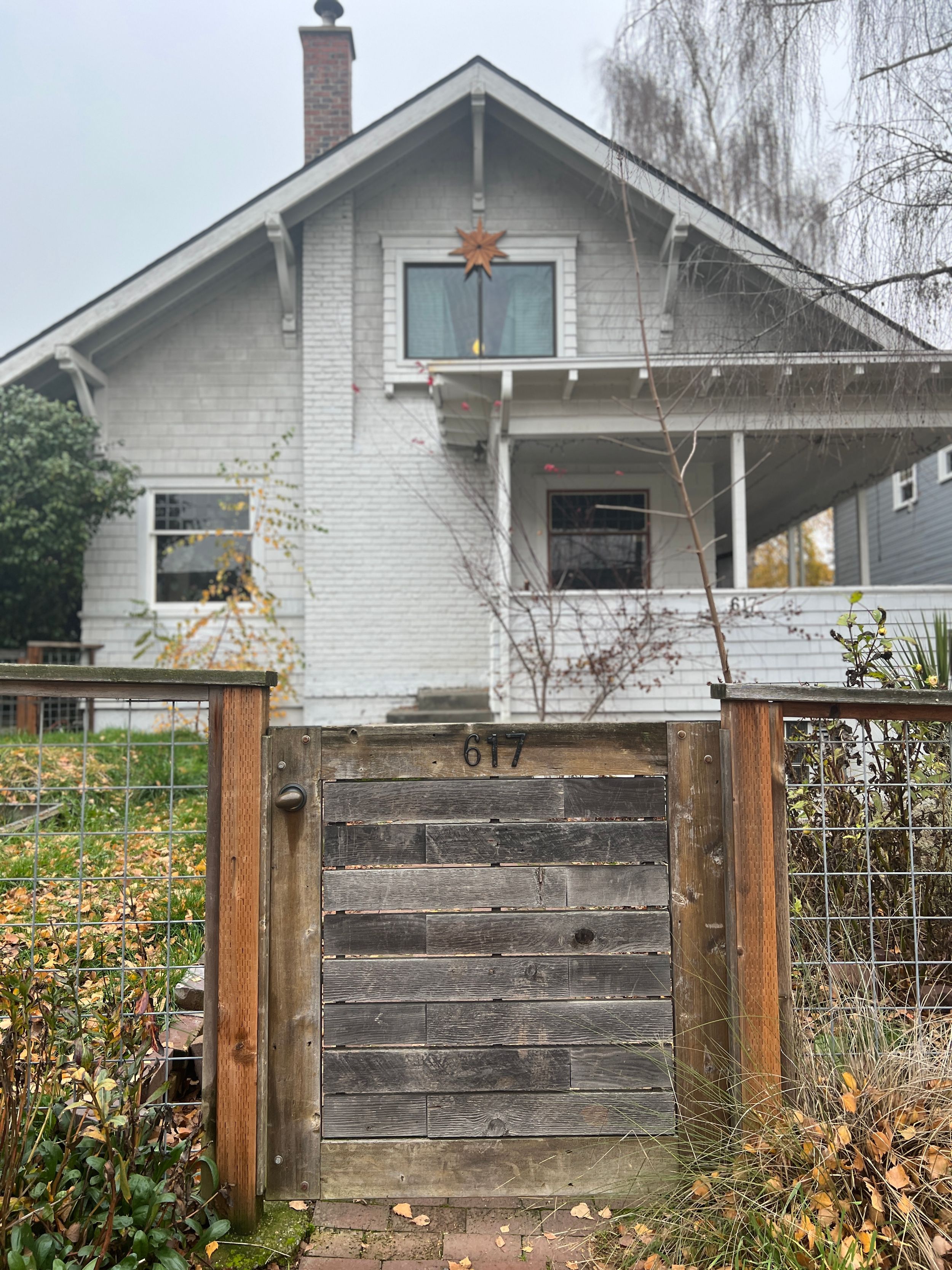 White craftsman house with rustic wooden fence and willow trees in the yard.