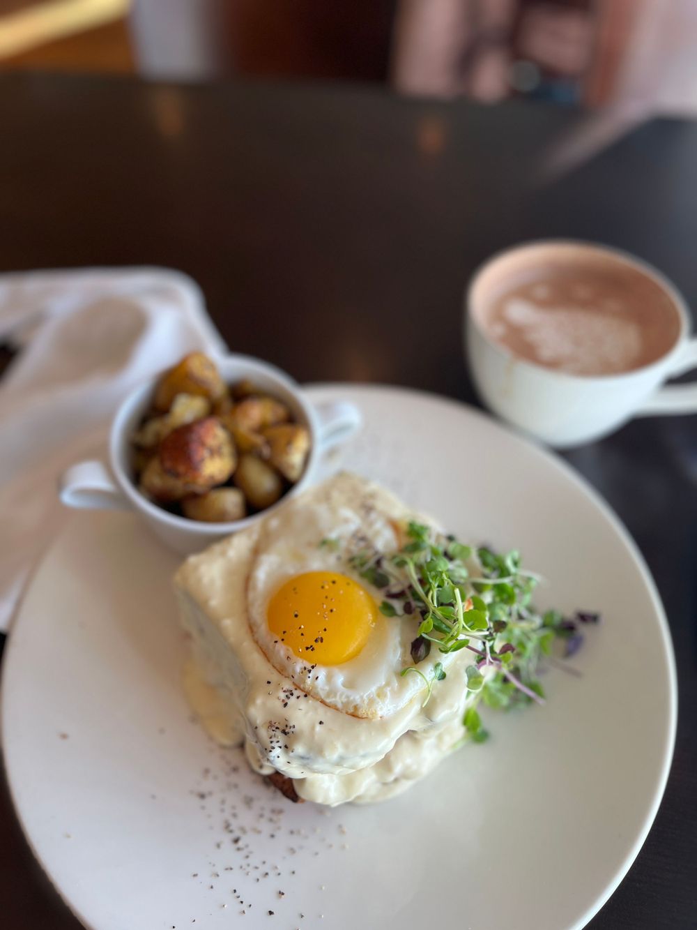 Brunch plate with sunny side up egg and microgreens served alongside a latte.
