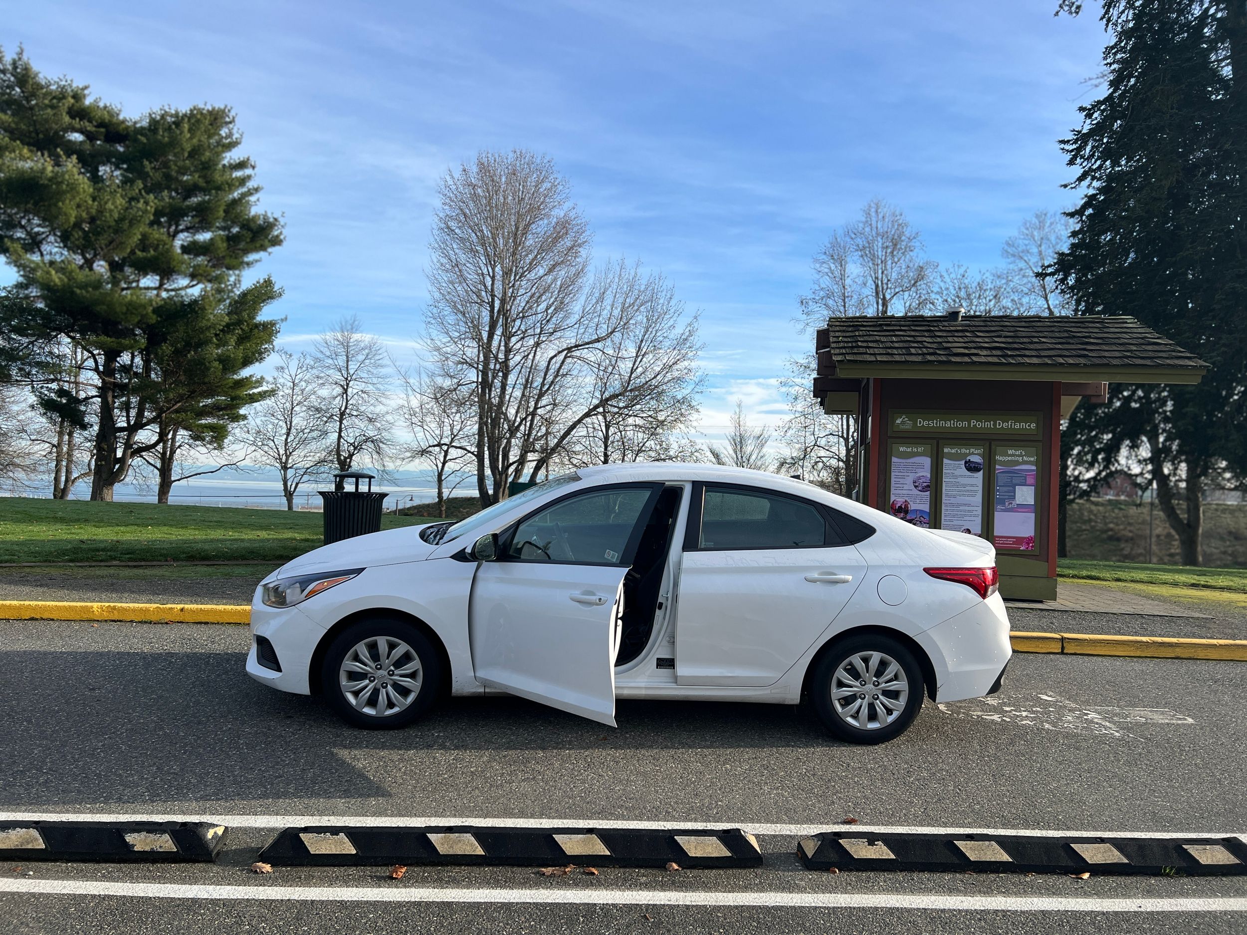 White sedan with door open parked on street near waterfront.