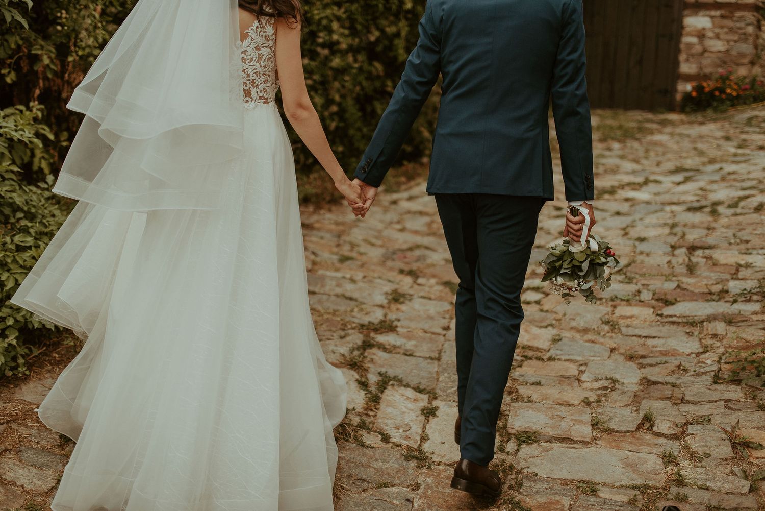 Wedding couple walking along a cobblestone path with flowing white dress.