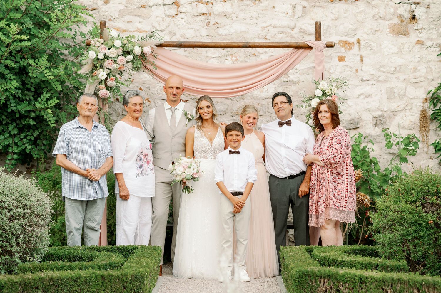 Wedding group photo with family members under a pink draped ceremony arch.
