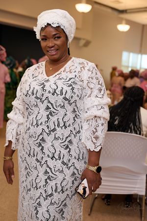 Woman wearing white lace traditional Nigerian dress and headwrap at formal event.