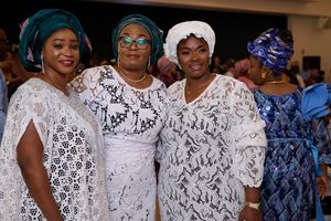 Three women in white lace and blue traditional Nigerian outfits posing together at celebration.