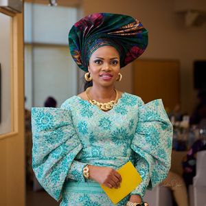 Traditional Nigerian wedding attire featuring a turquoise lace dress with puffy sleeves and a colorful gele headwrap.