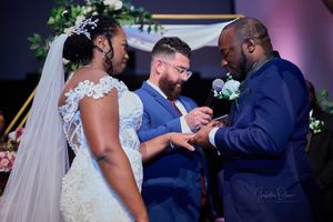 Ring exchange ceremony during wedding with officiant in navy suit.
