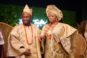 Couple in traditional Nigerian wedding attire with coral beads against green wall backdrop.