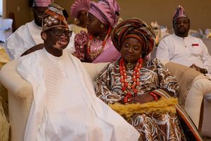Traditional Nigerian wedding guests in colorful attire and headwraps seated during celebration ceremony.