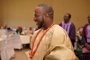 Guest wearing cream colored traditional agbada and coral beads smiling at Nigerian celebration.