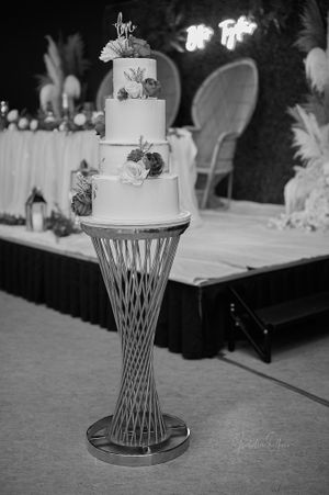 Elegant white wedding cake displayed on modern silver pedestal with floral decorations.