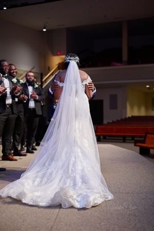 Back view of bride in flowing white gown with long veil during ceremony.