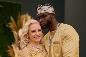 Couple in formal attire posing against greenery backdrop at wedding celebration.