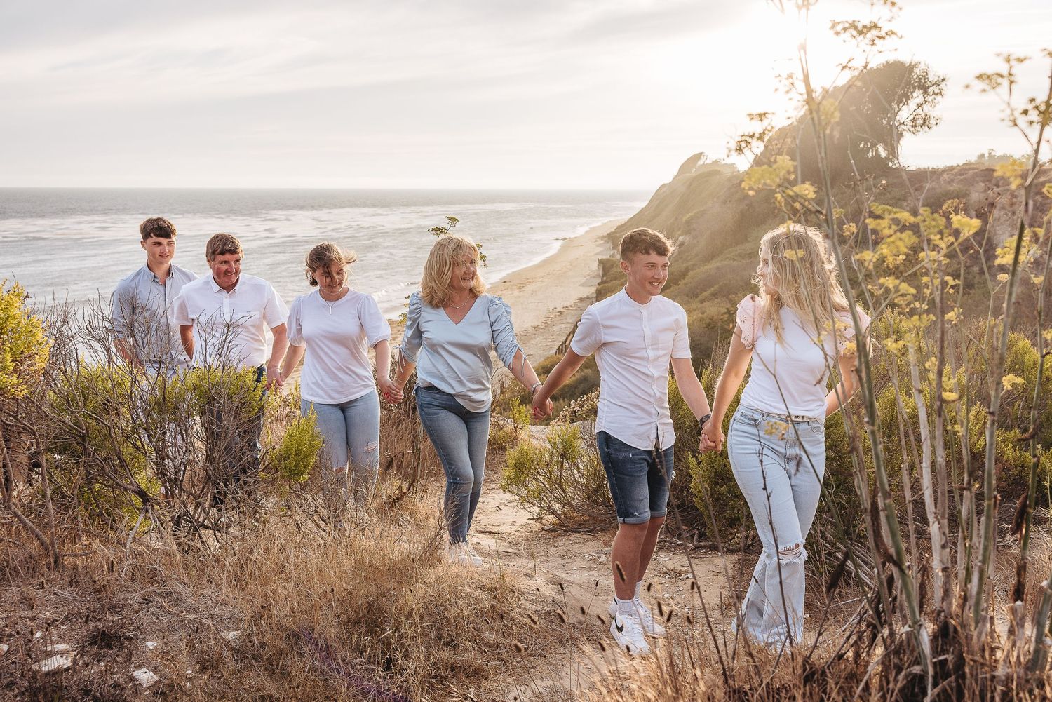 Group walking along a coastal trail at sunset through brush and trees.