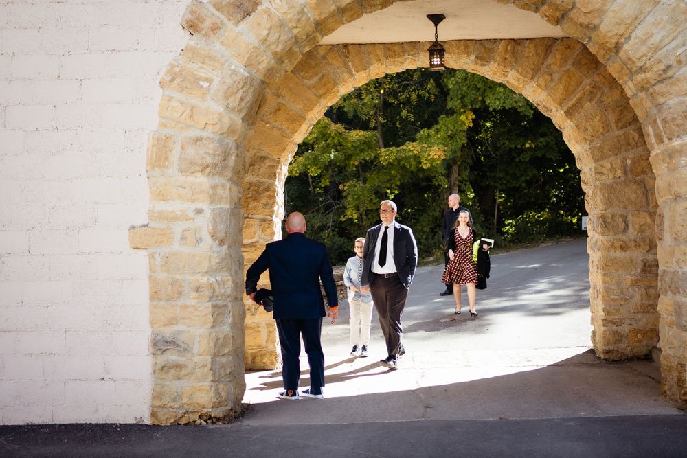 People walking through a stone archway passage on a sunny day.