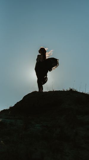 Silhouette stands on hilltop against backlit sky creating dramatic sunset pose.