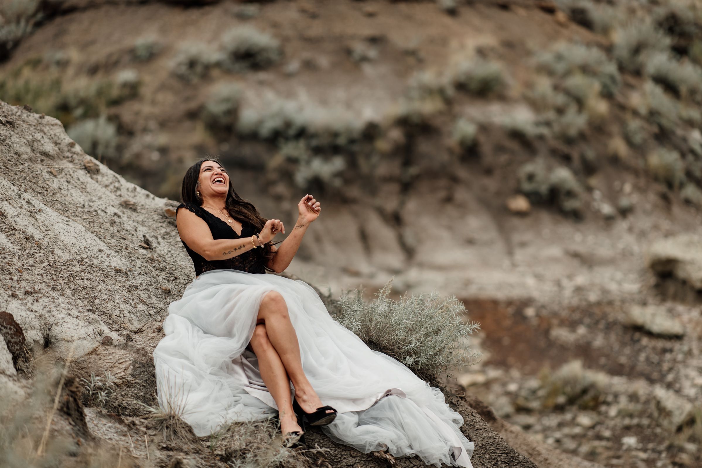 Person in formal attire poses on rocky terrain during outdoor photo session laughing.