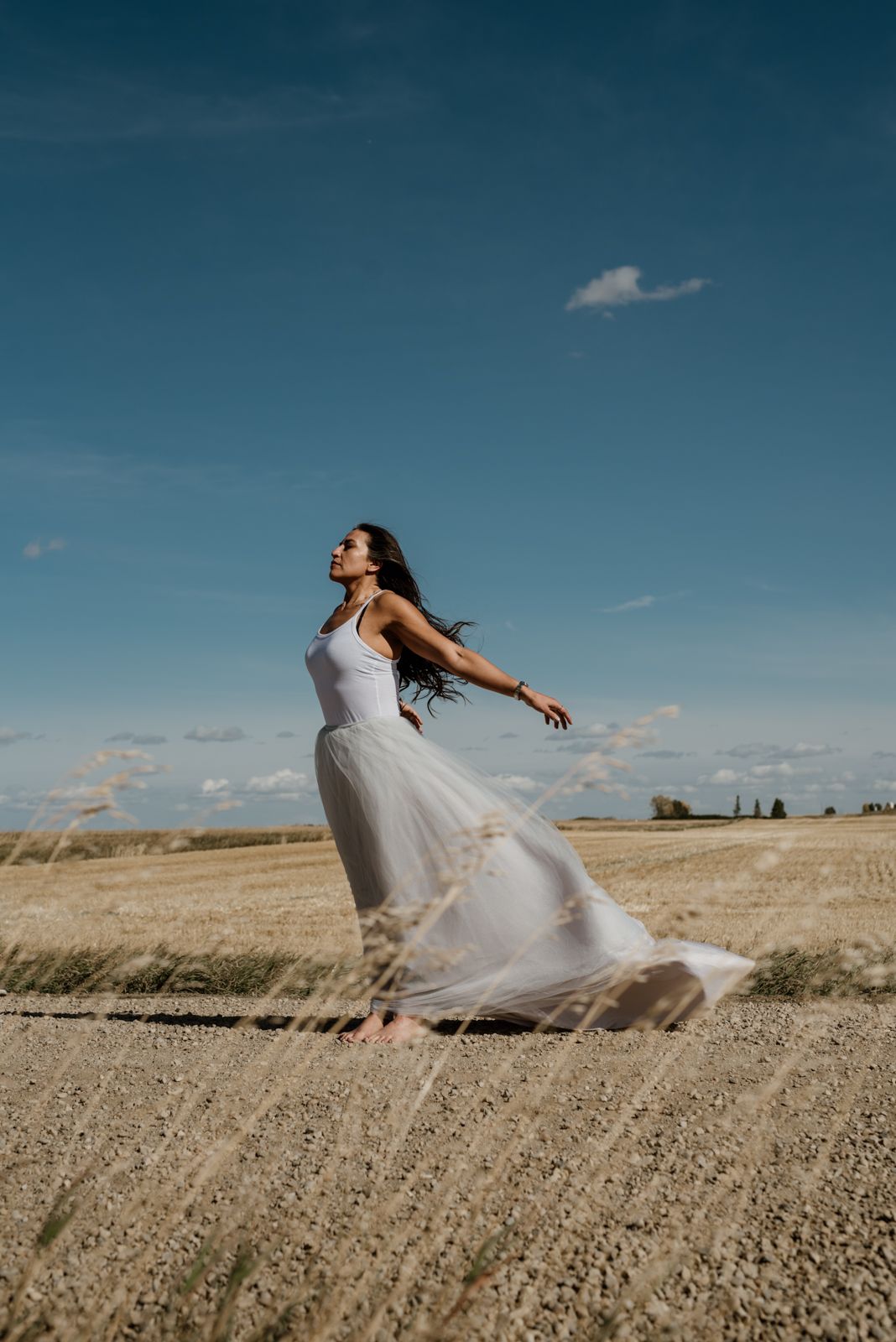 Woman in white dress twirls gracefully in open field under bright blue sky.