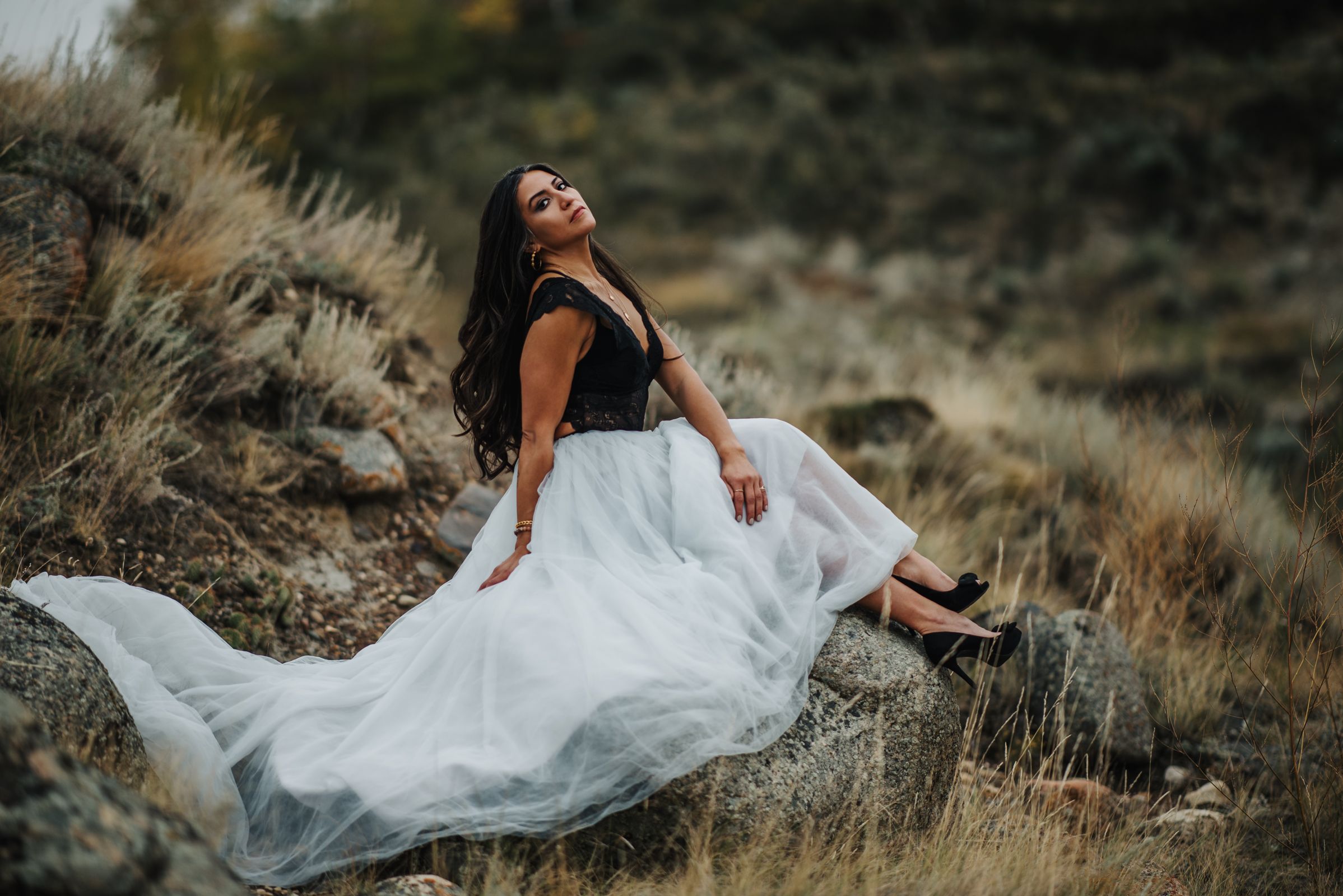 Person in black top and white skirt reclines on hillside during sunset photo session.