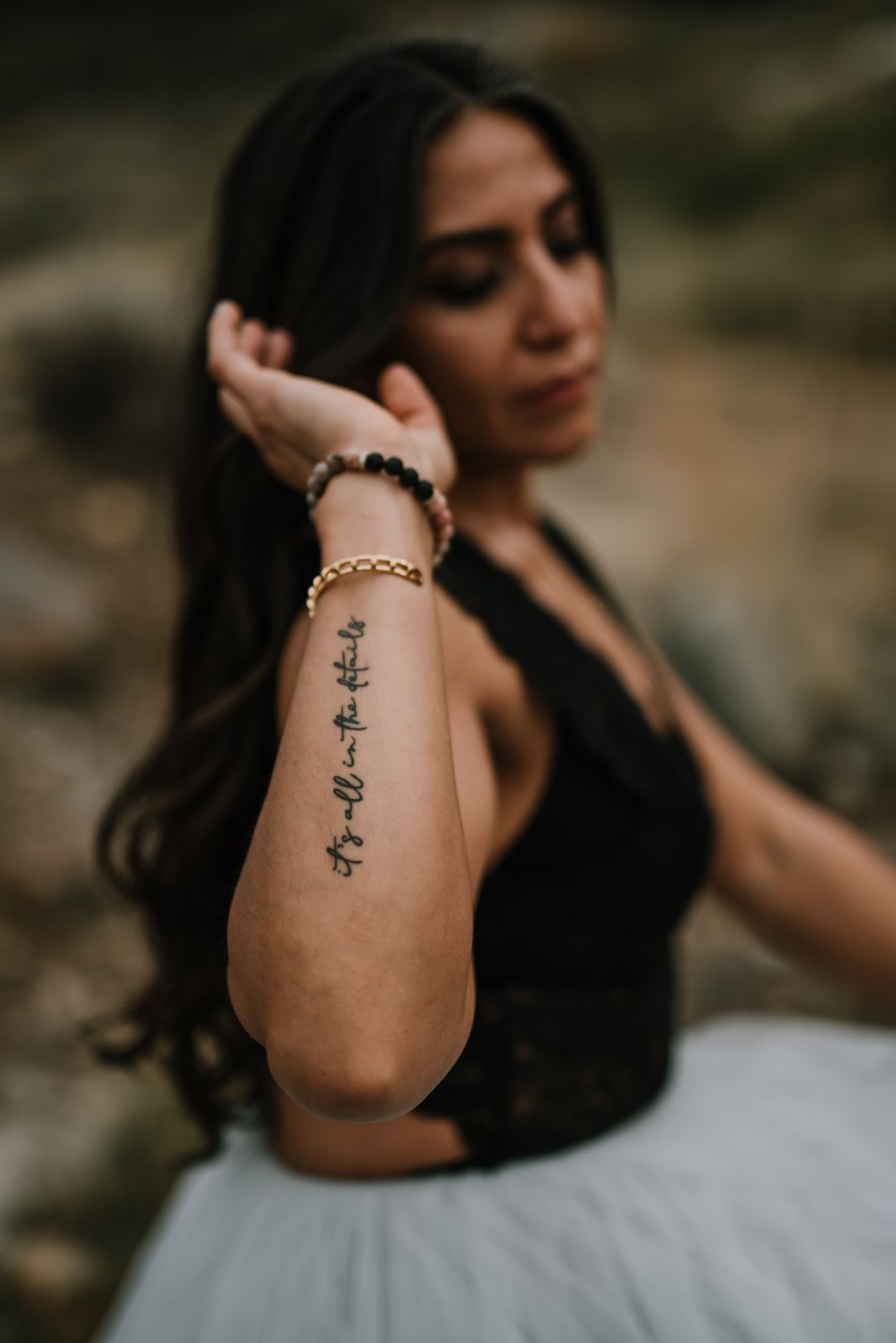 Close-up of artistic arm tattoo against dark clothing and natural background.