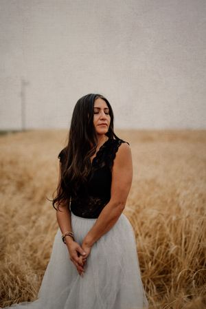 Figure in black top and light skirt poses in golden wheat field at sunset.