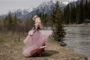 A flowing pink tulle dress twirls against a mountainous backdrop with evergreen trees and a river.