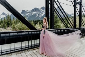 Pink tulle dress flows dramatically on wooden bridge with mountain peaks in background.