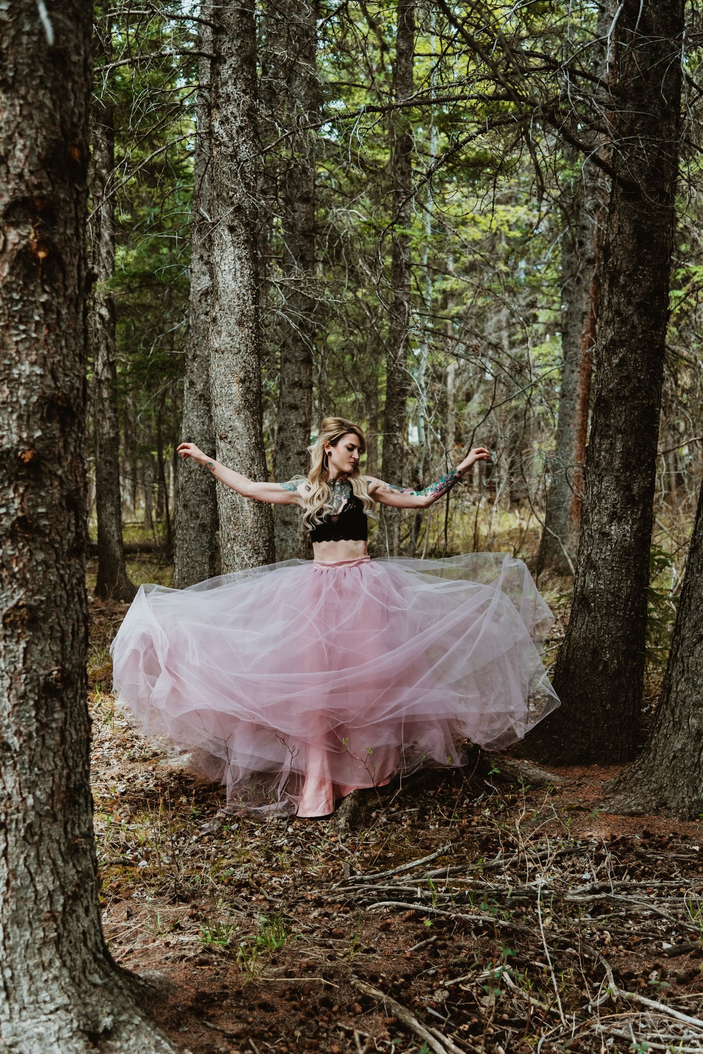 Flowing pink tulle skirt twirls through forest of tall pine trees.