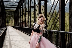 Vintage bridge frames figure in pink tulle skirt against mountain landscape.