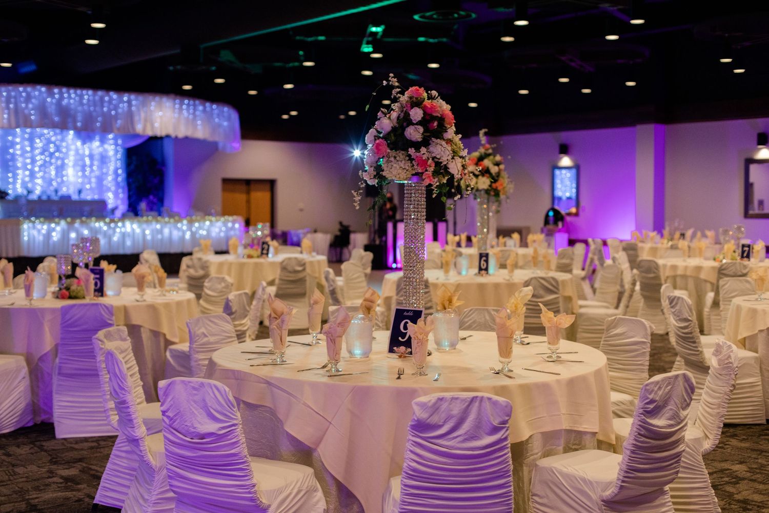 An elegant wedding reception venue with purple lighting and white-clothed tables.