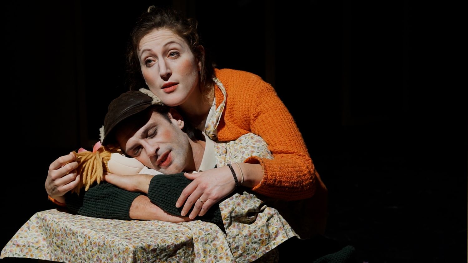 Two performers in a theatrical scene on stage with dramatic lighting.