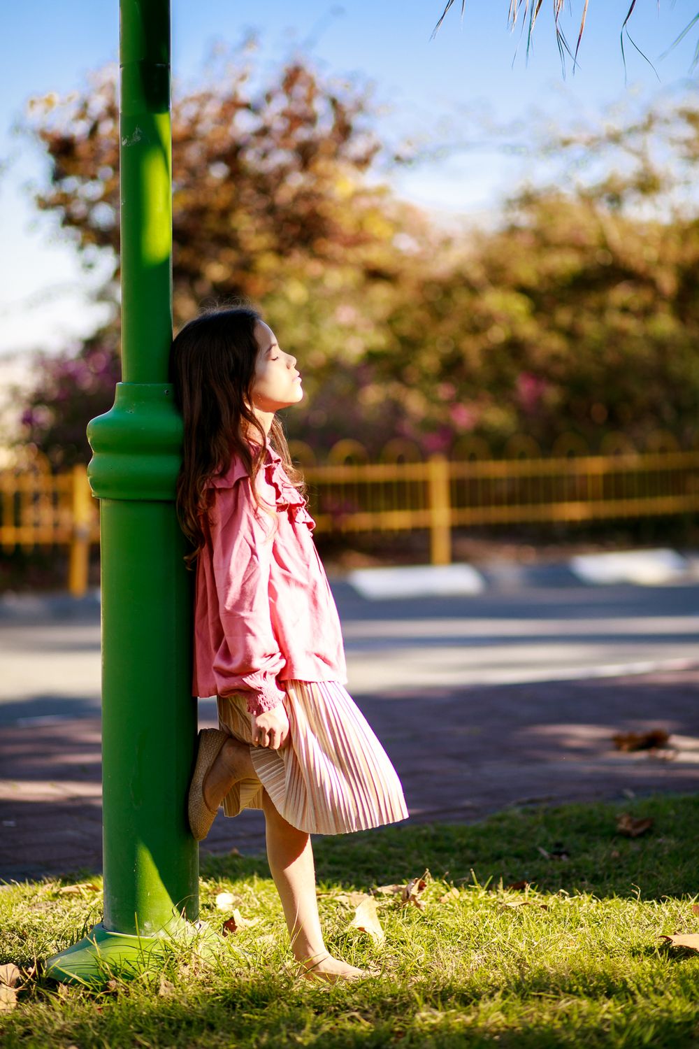A picture of a girl leaning on a pole and basking in the sun