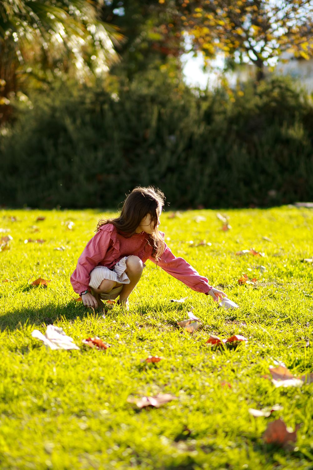A picture of a beautiful girl picking up fallen leaves from the grass