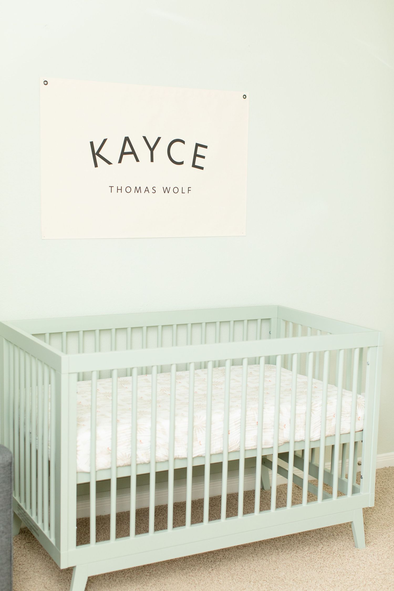 Minimalist nursery with mint green crib and name sign on wall.