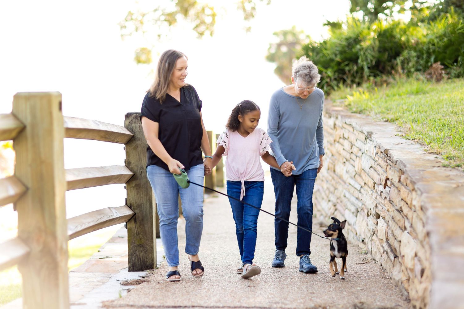 A family walks together with their small dog on a stone path outdoors.