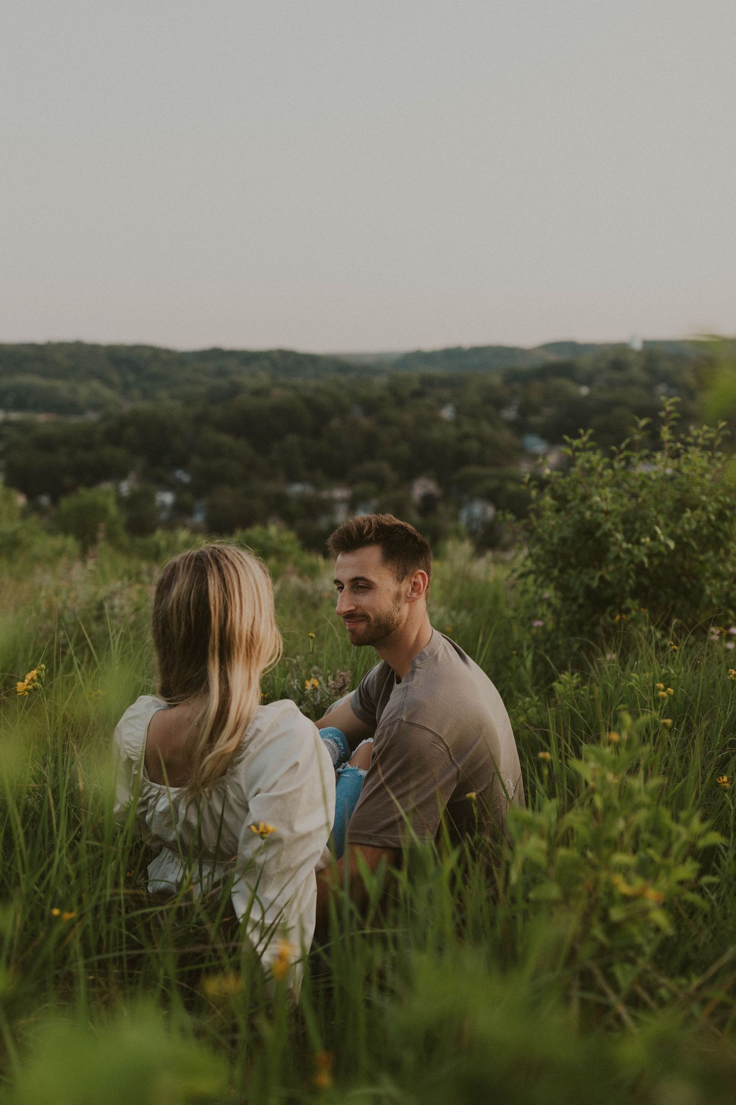 Couple sitting together in a lush green meadow during golden hour.