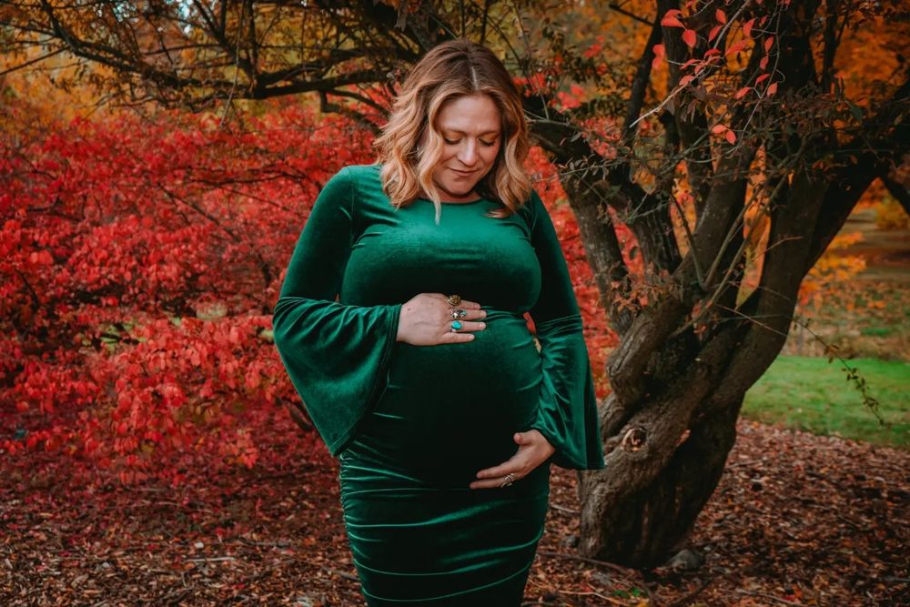 Autumn maternity photo in emerald velvet dress with vibrant red foliage.