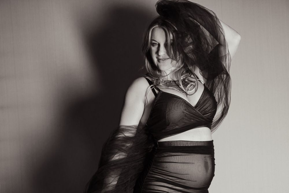 Artistic black and white boudoir photo featuring dramatic shadows and curves in dark attire.