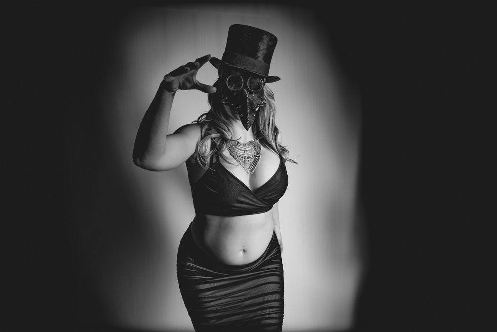 Black and white maternity photo with vintage top hat and dramatic lighting.