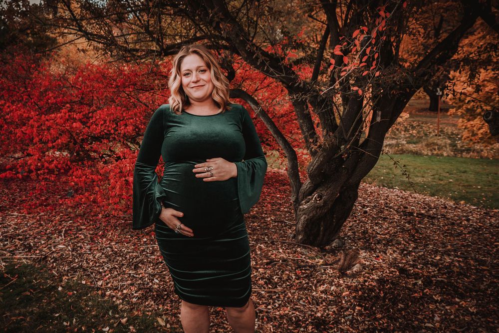 Maternity photo with red maple tree and fallen leaves in autumn setting.