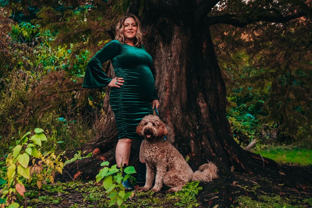 Maternity portrait in green dress with goldendoodle dog by large tree.