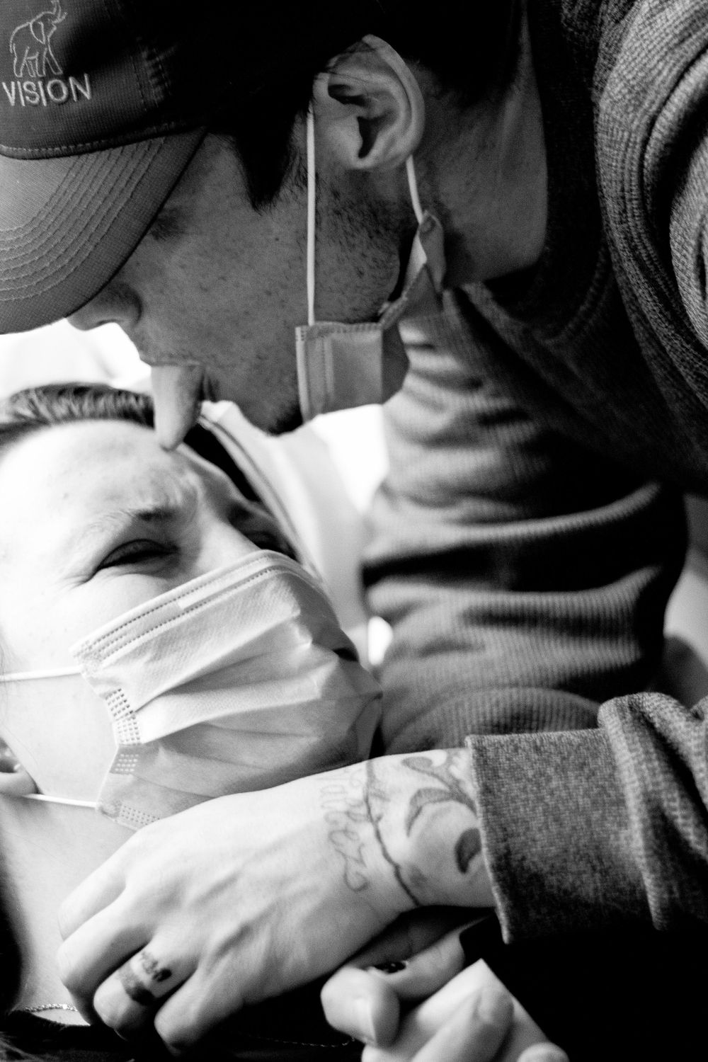 Black and white image showing an intimate moment between mother and father-to-be, with the him sticking his tongue onto the her forehead.
