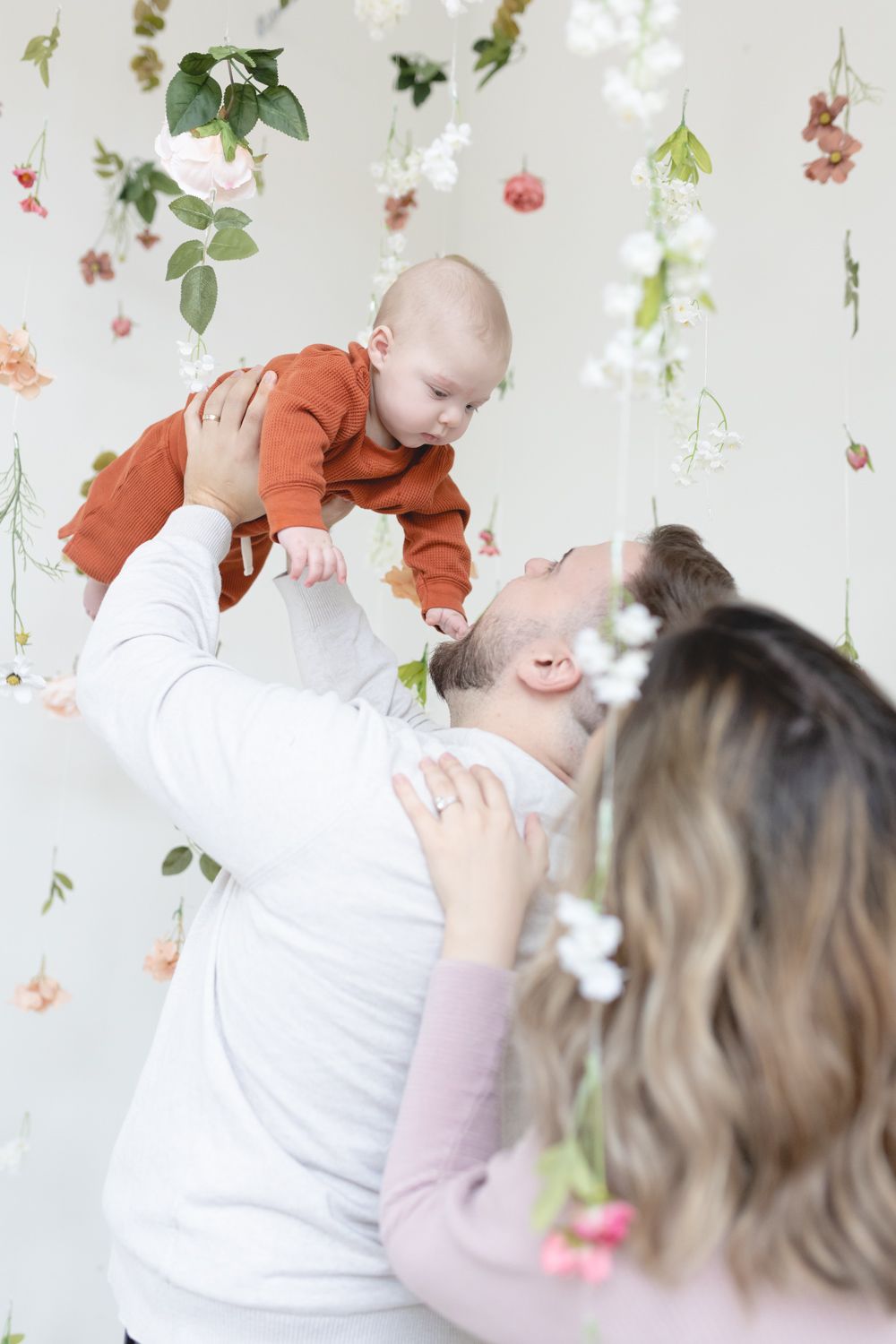 A joyful family moment captured in front of a delicate floral backdrop with hanging garden decorations.
