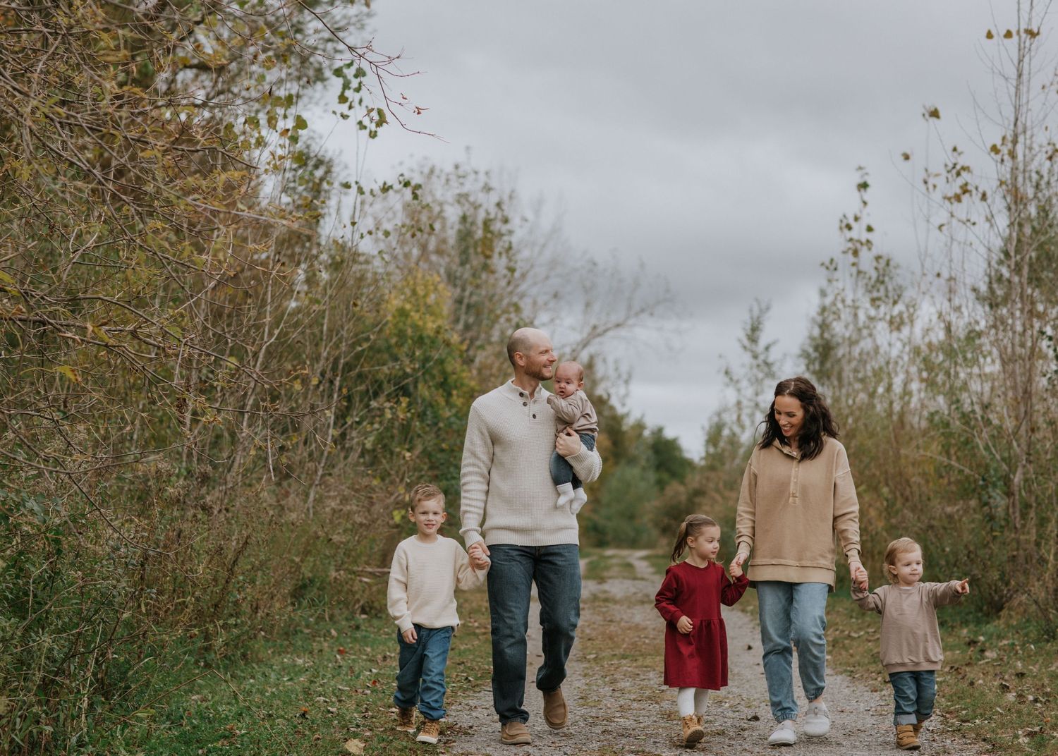 A family walks together on a rustic path during a cloudy fall day.