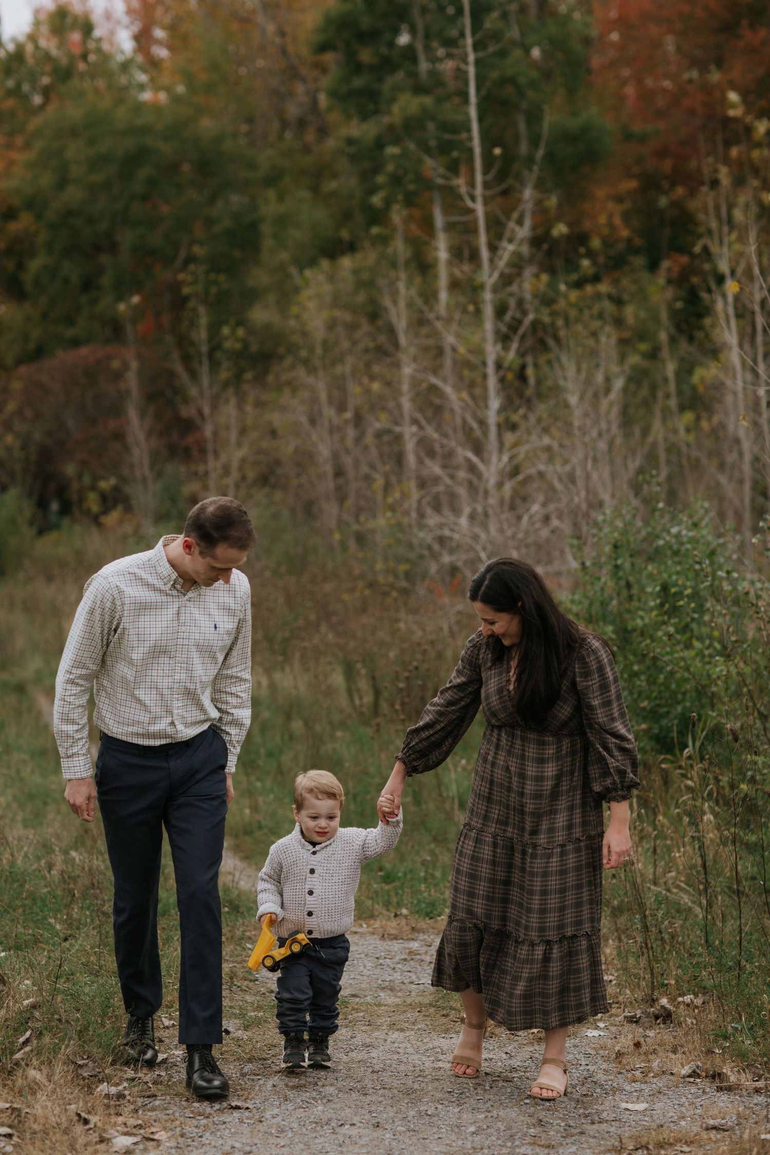 A family walks together on a forest path during fall while holding hands.