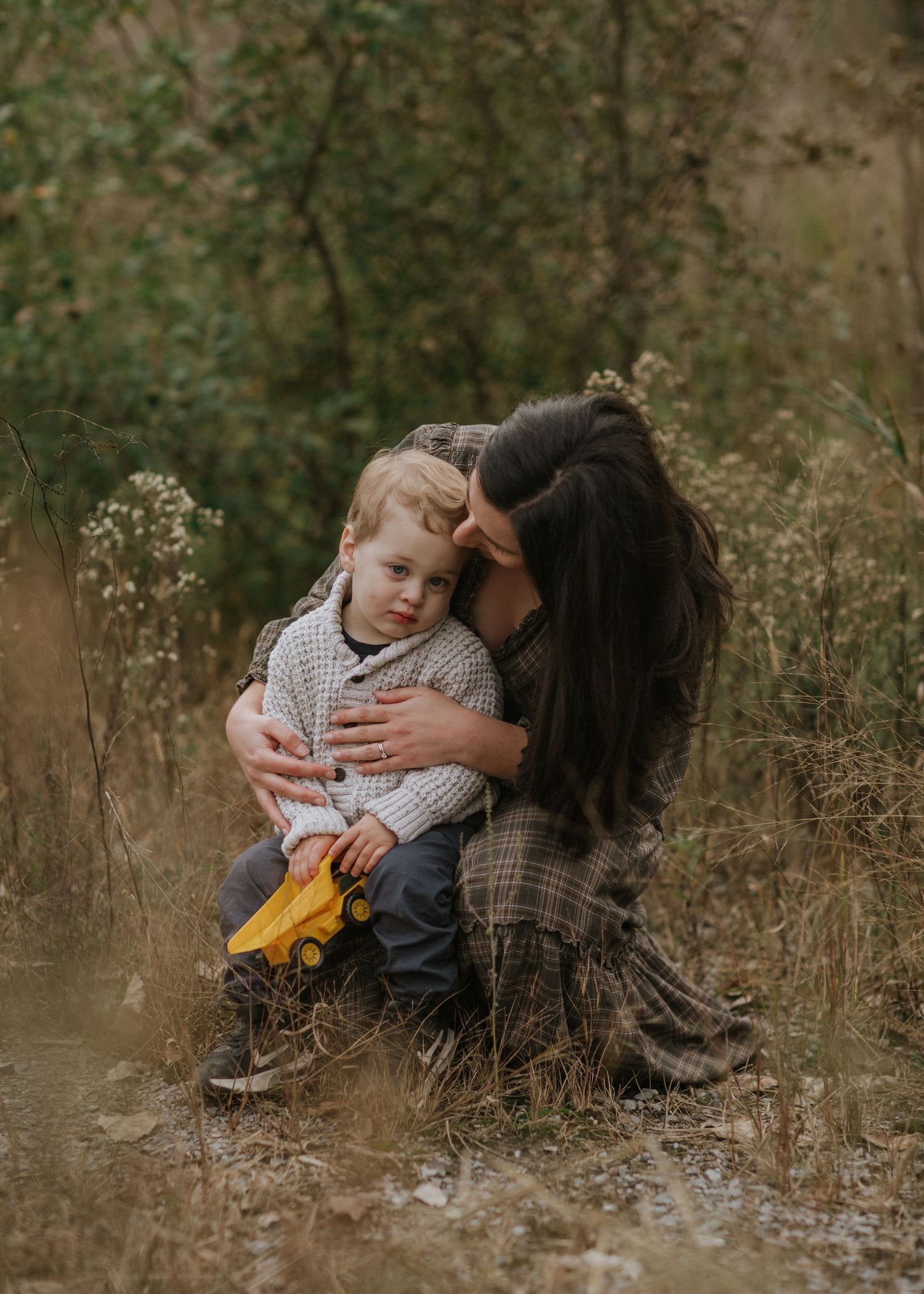 A tender moment captured between parent and child amid tall grass in an autumn field.