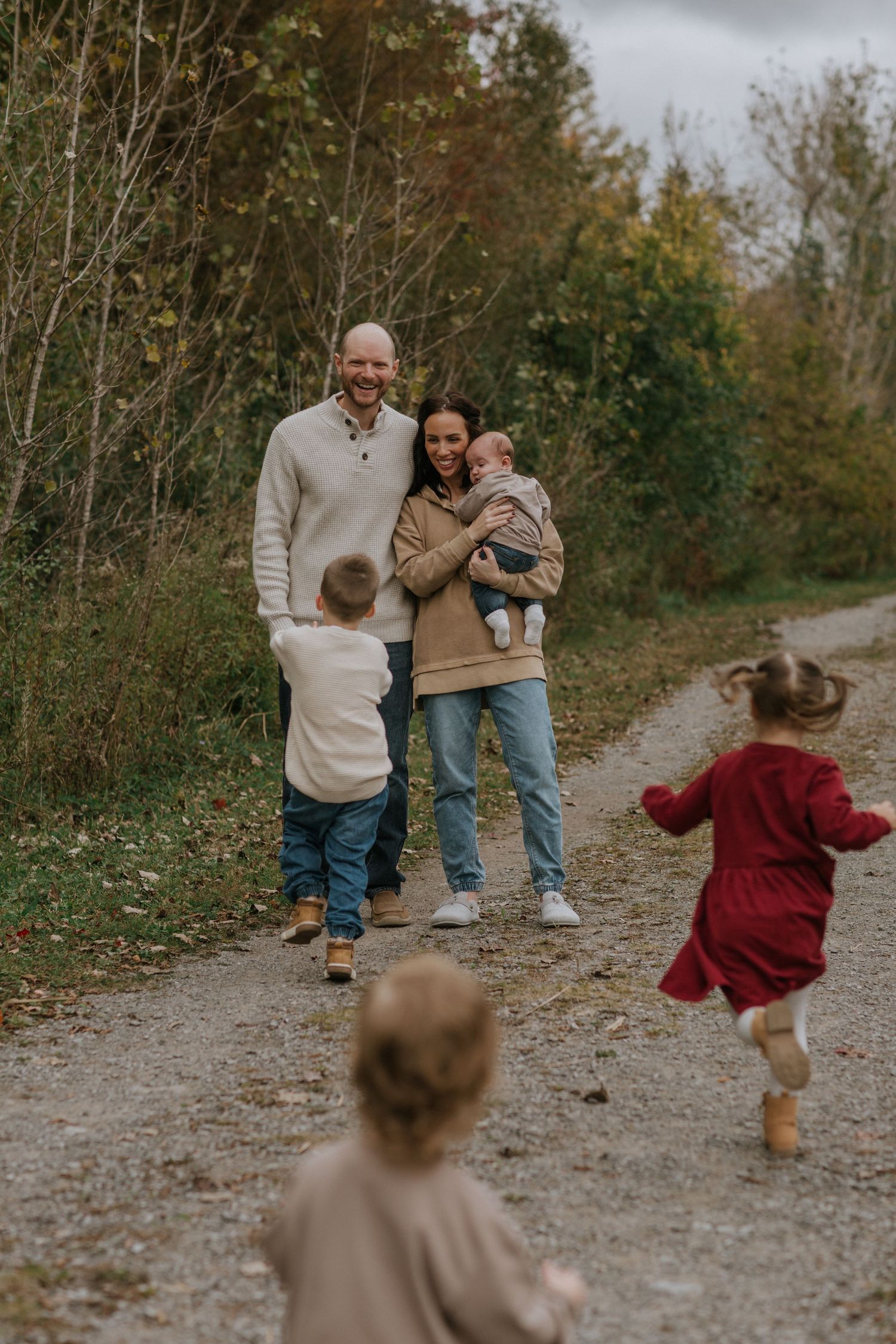 Children run playfully toward their parents on a scenic autumn walking trail.