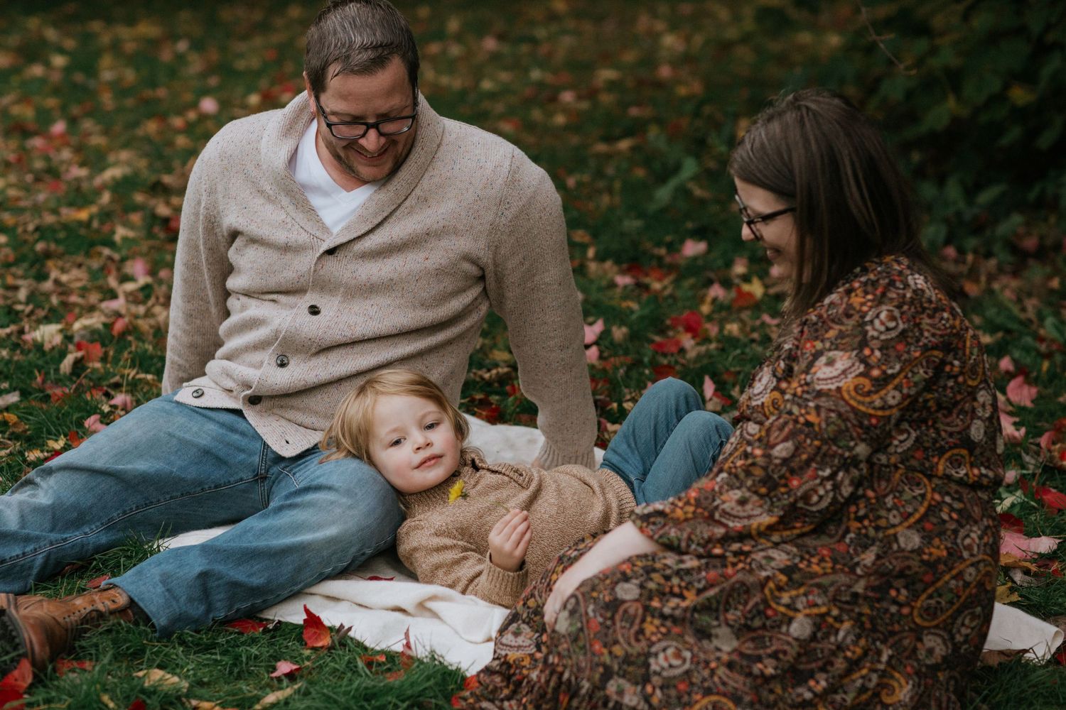 A family relaxes on a blanket outdoors during autumn with scattered leaves on the ground.