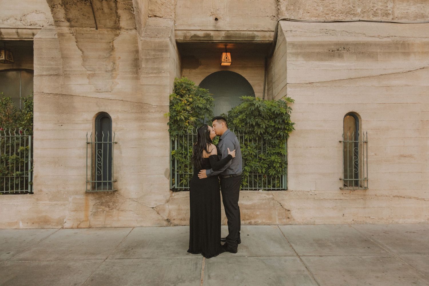 Elegant couple embracing outside historic stone building with arched doorways.