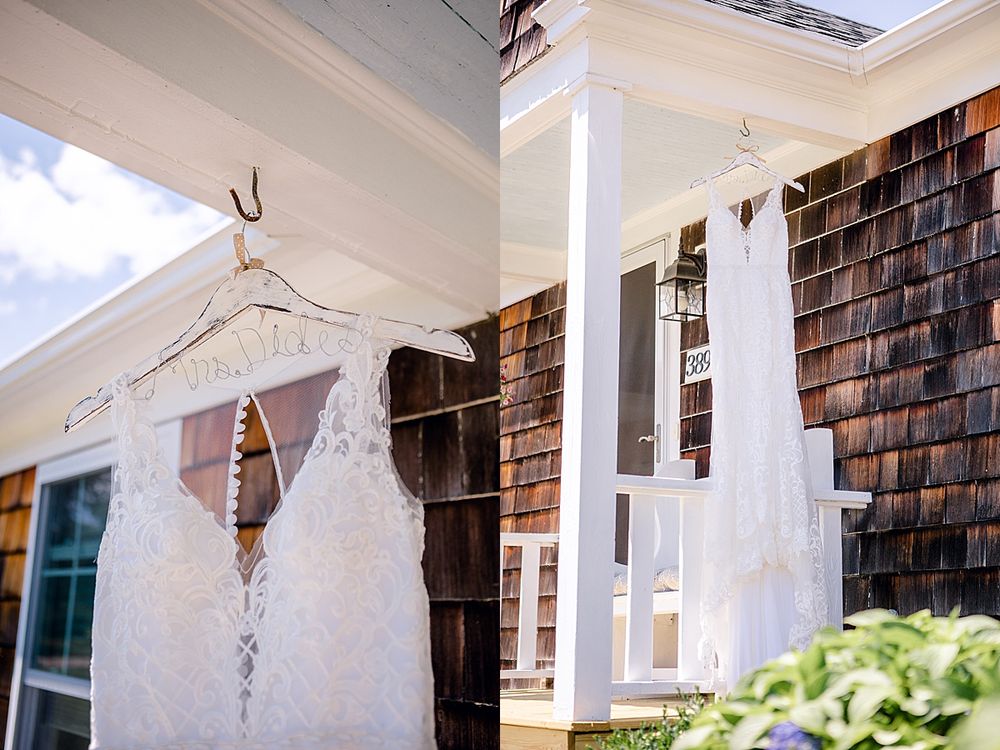 White lace wedding dress hanging on display against cedar shake siding of a house.