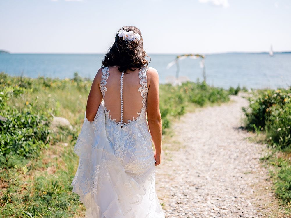 Wedding dress with detailed lace back detail on beach path leading to an arch.