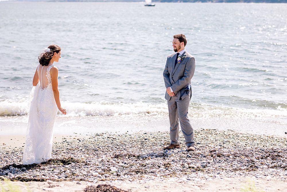 Beach wedding couple standing on rocky shoreline with ocean waves in background.